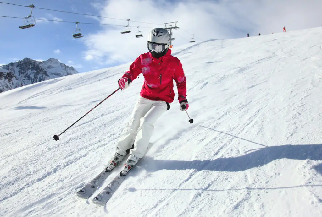 Las mejores chaquetas de esquí para mujer: mujer esquiando con chaqueta roja con telesilla al fondo